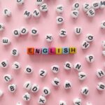 Scattered letter beads form the word 'English' on a pink background, symbolizing language learning.