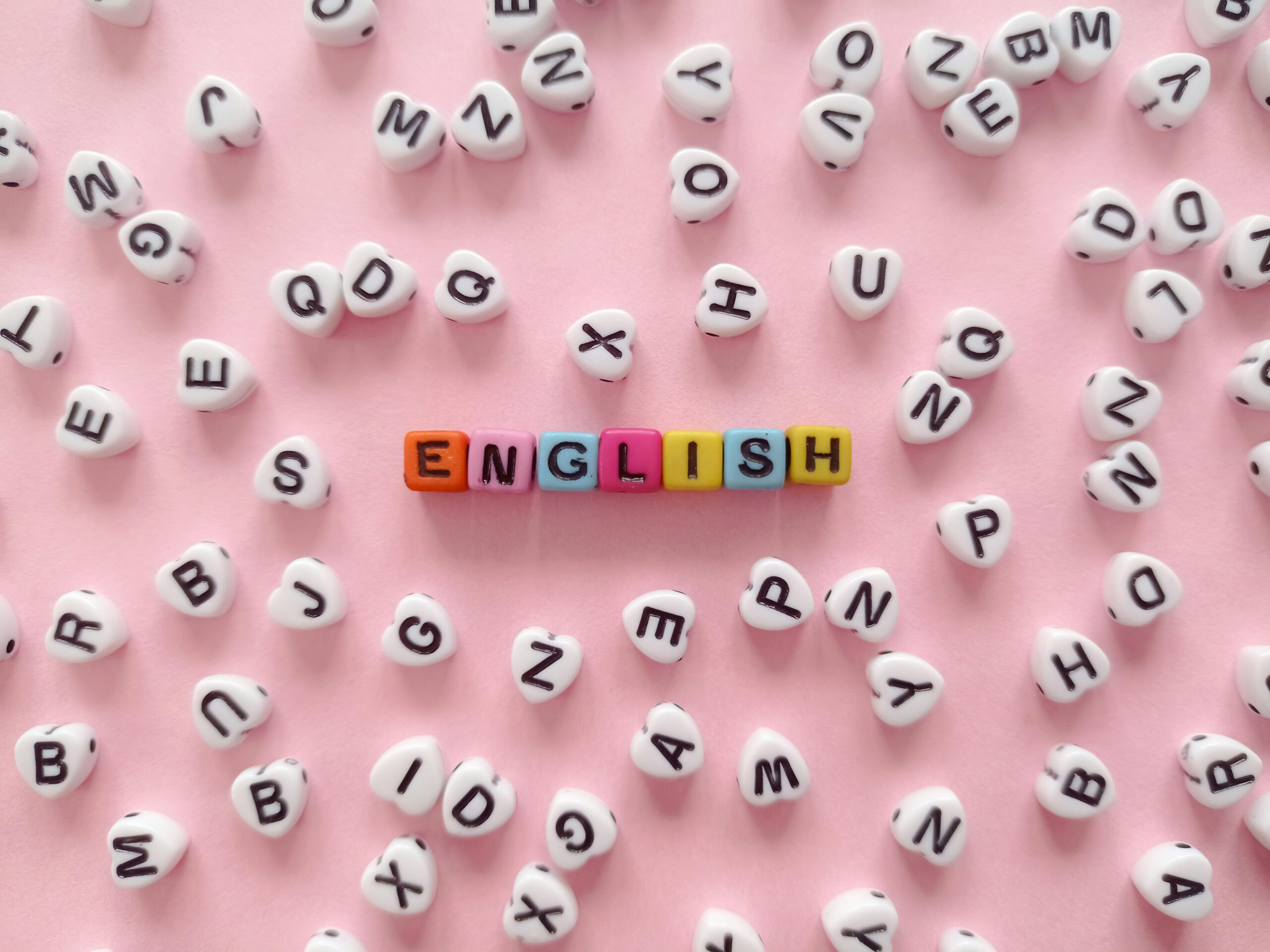Scattered letter beads form the word 'English' on a pink background, symbolizing language learning.