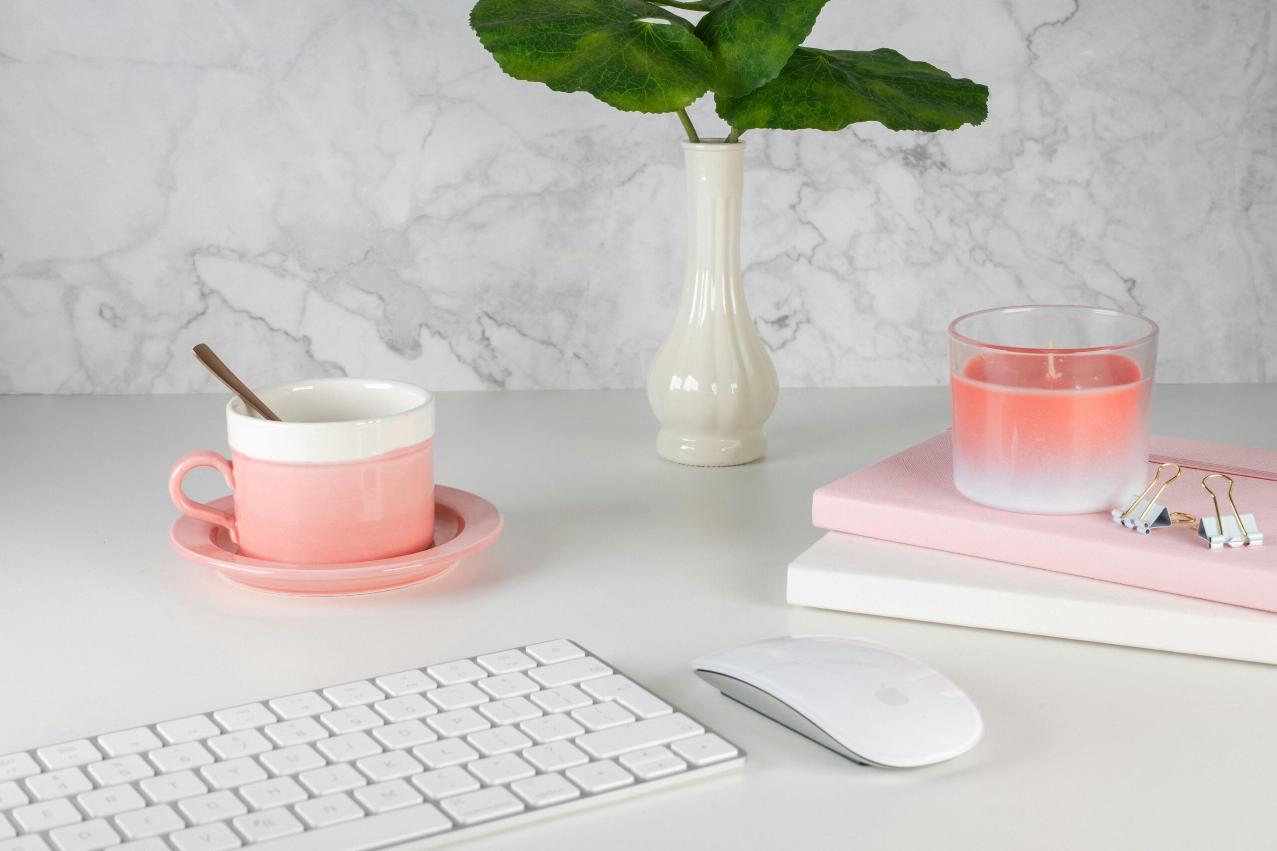 Stylish office workspace featuring a pink cup, candle, and plant on a modern desk.